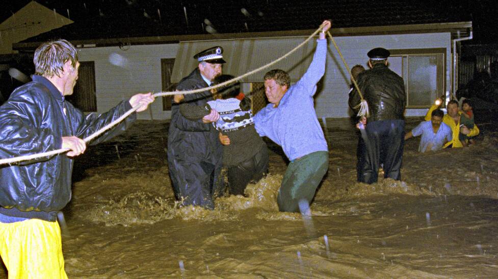 Police and workers help a family to safety from their flooding house in The Avenue, Figtree. Picture: file.
