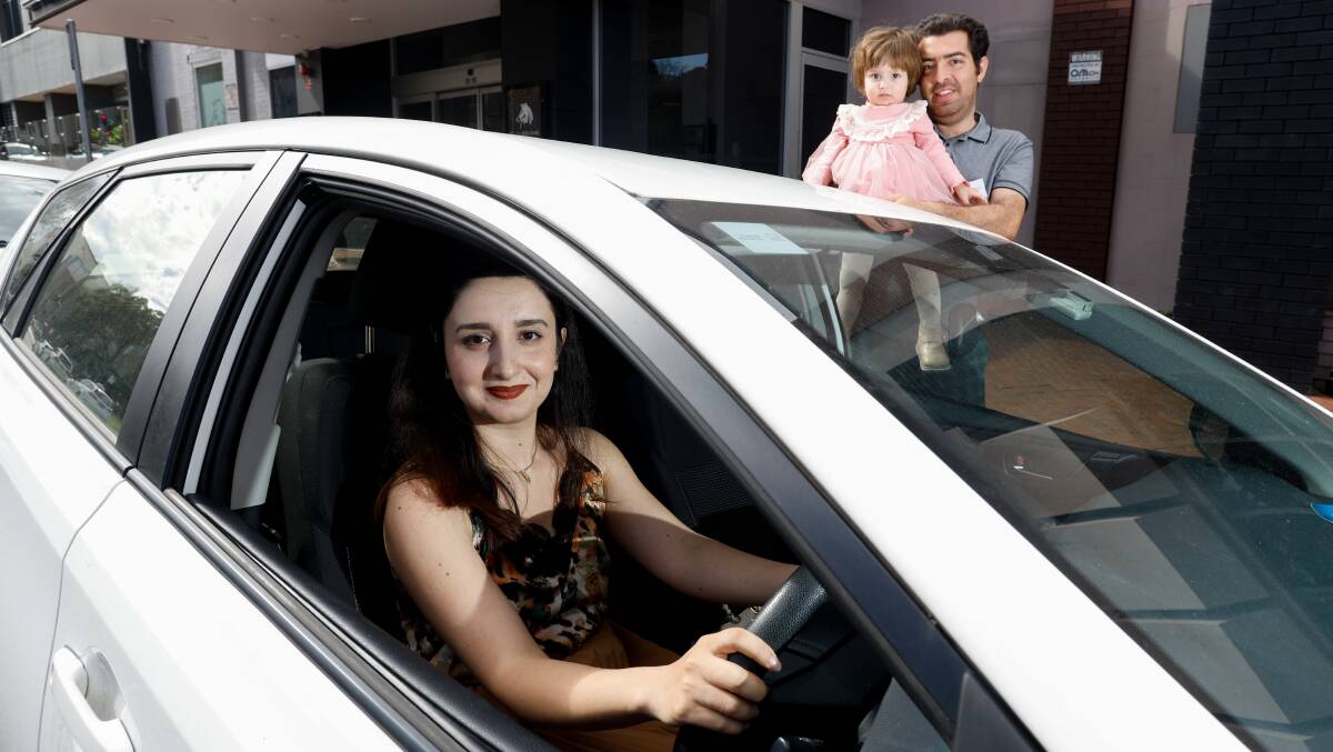Mahnaz Darabi, can now get behind the wheel after obtaining her licence through a refugee driver's licence program. In the background her husband Esmaeil Taslimi, also part of the program, holds their 18-month-old daughter Regina Taslimi. Picture by Anna Warr