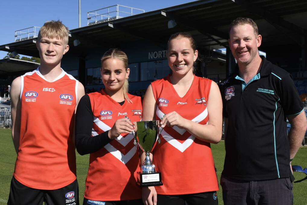 Illawarra Storm players Harrison McDonald, Montana Doubell and Chloe Aivaliotis proudly receive the Simon Smyth Cup from AFL staff member Simon Smyth. Picture - AFL North Coast