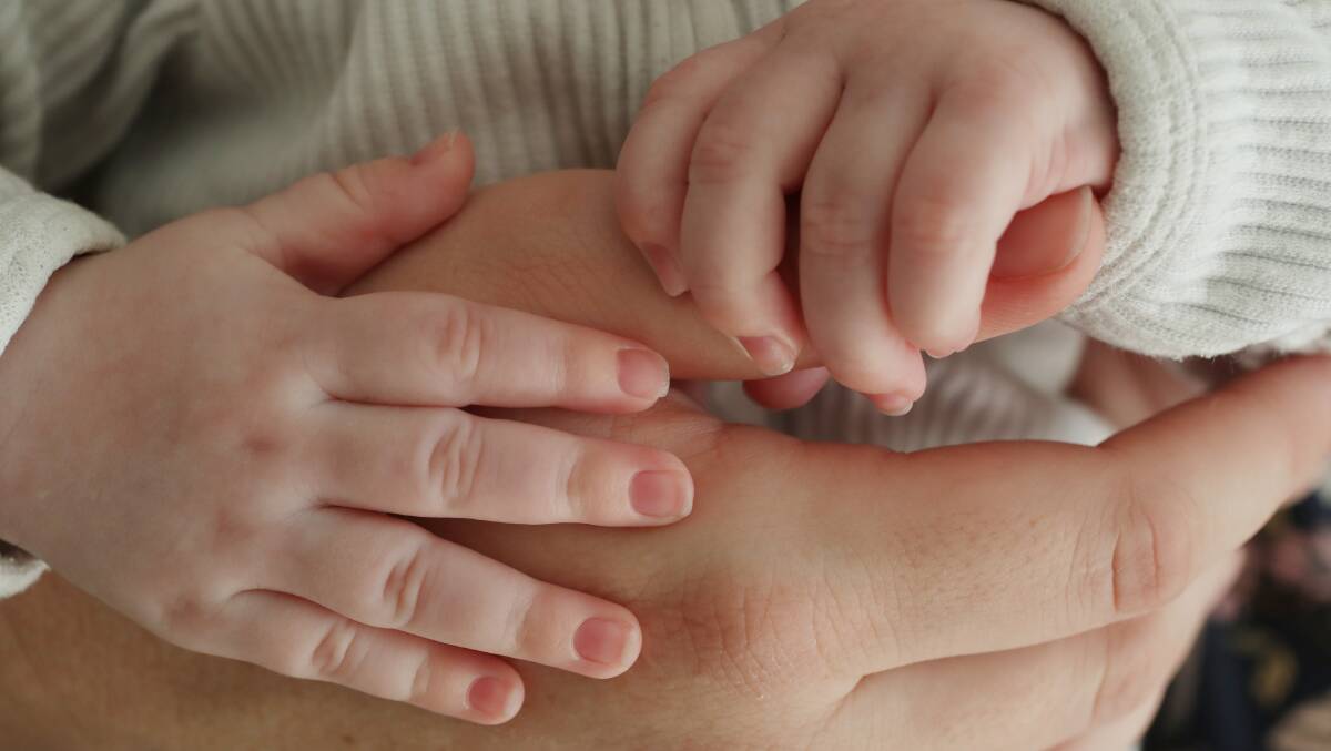 A baby's hands grip hold of his mother's thumb. File picture