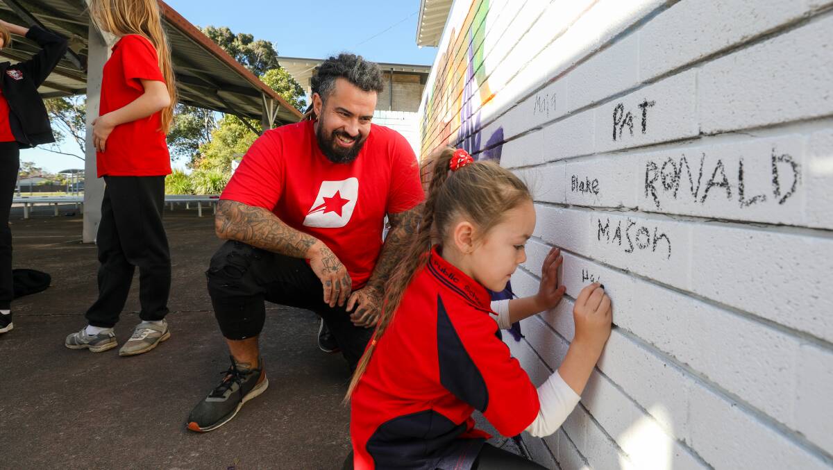 Kids are invited to write their names on the murals that artist Danny Mulyono is painting on their school walls, to give them ownership over the project. Picture by Adam McLean.