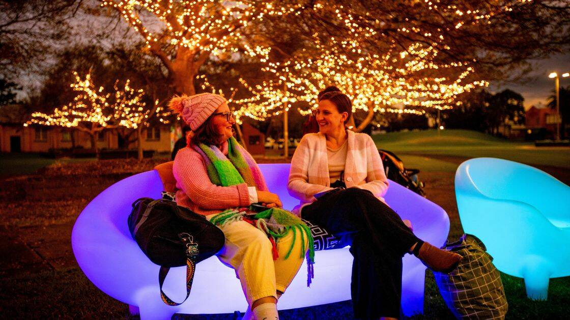 Women sit on glowing seats near fairy lights in MacCabe Park. Picture from Wollongong City Council