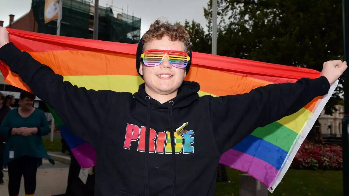A file picture of a young person holding a rainbow flag and wearing a Pride jumper. 